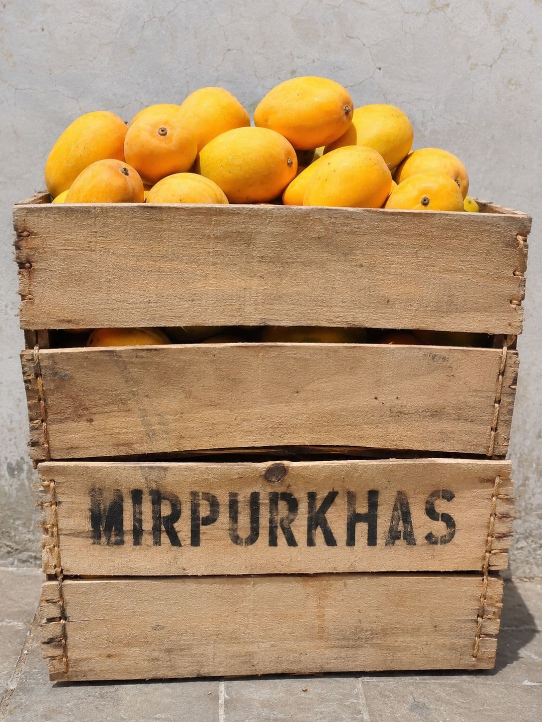 A wooden fruit crate stencilled with the word MIRPURKHAS, holding fruit wrapped in paper.