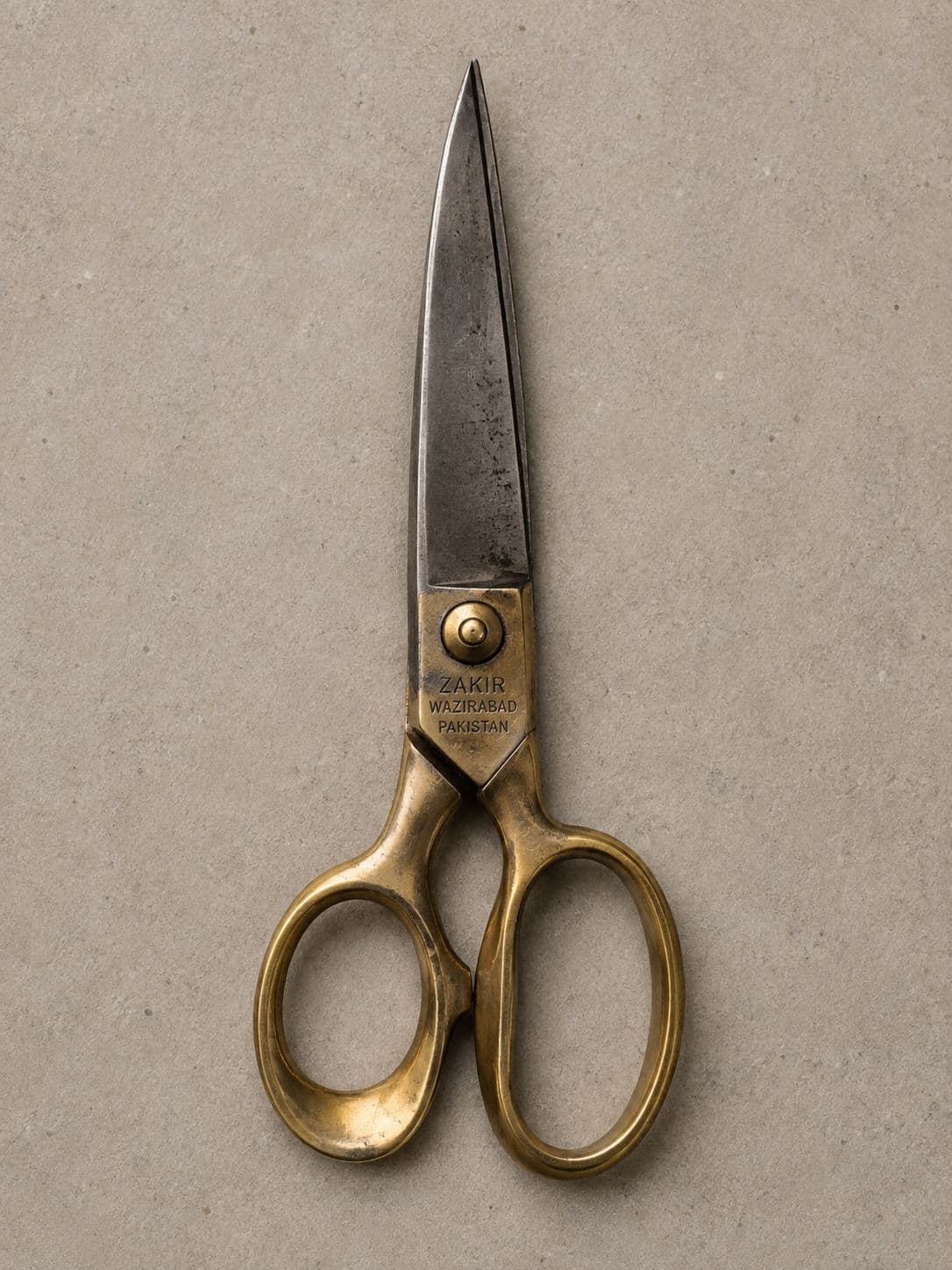 A pair of large brass-handled tailor's shears lying open on a pale surface.